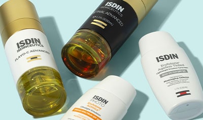 A smattering of ISDIN products lay on a blue background. There are two sunscreens, a vitamin C serum, and a retinoid serum.