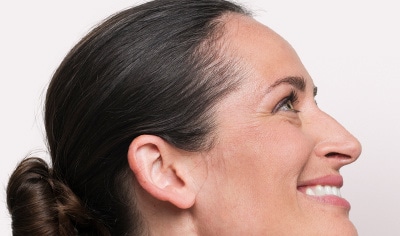 A light-skinned brunette model in profile, smiling with hair styled in a bun.