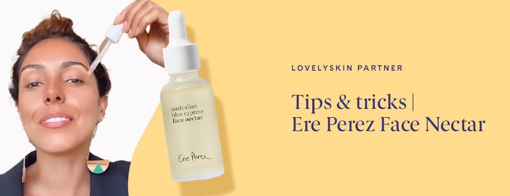 A woman with a medium skin tone and short brown hair drops Ere Perez Australian Blue Cypress Face Nectar onto her cheek.