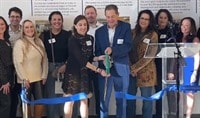 A group of people smiling and cutting a big blue ribbon.