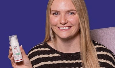 Woman with long blonde hair and fair skin holds a white bottle of sunscreen.
