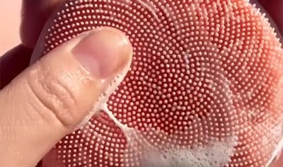 A hand holding a coral device with silicone touchpoints and soap suds.