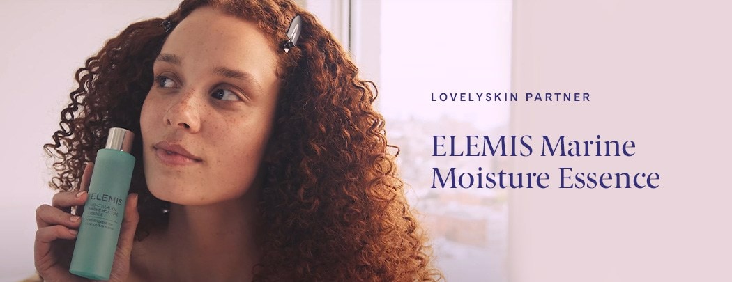 A woman with freckles and red curly hair looking into the distance and holding a bottle of ELEMIS Marine Moisture Essence toner.