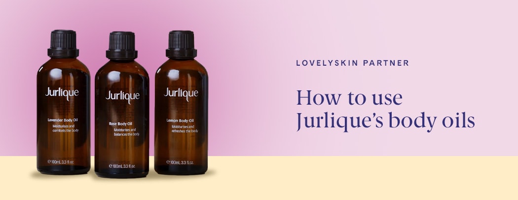 Three Jurlique Body Oils in natural brown glass sit next to one another on a yellow table with a pink background.