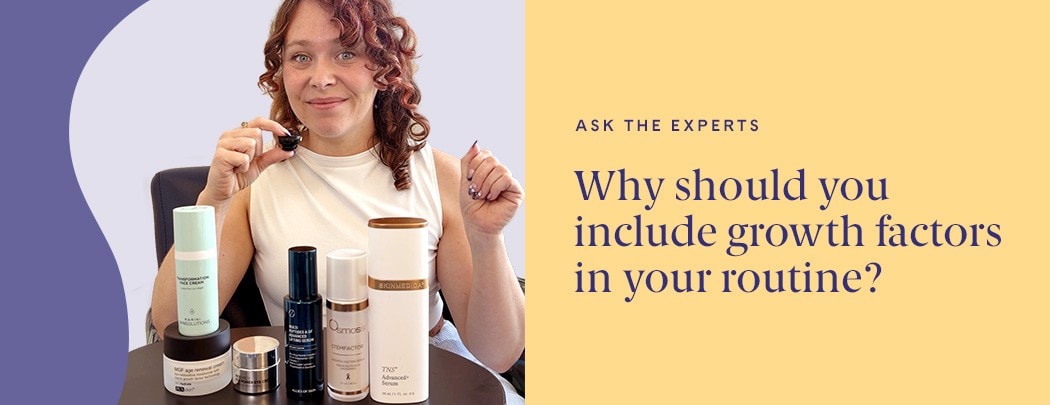 A woman with fair skin and red hair holds a small microphone while sitting behind an array of growth factor skin care products.