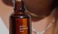 A person with a light to medium skin tone holds a bottle of Ere Perez Guava Gradual Face Tan with the dropper hovering over the open bottle.