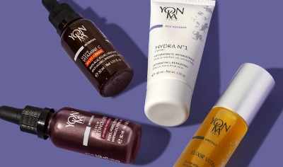 Four products, one in a white tube, two in clear glass bottles, and one in a brown glass bottle, lay on a medium purple background.