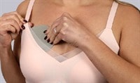 A person wearing a soft pink bra and a medium skin tone holds a Joylux coldHER Cooling Bra Insert over their breast.