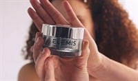 A black woman with curly hair holding a jar of ELEMIS Pro Collagen Night Cream in front of her outstretched palm.