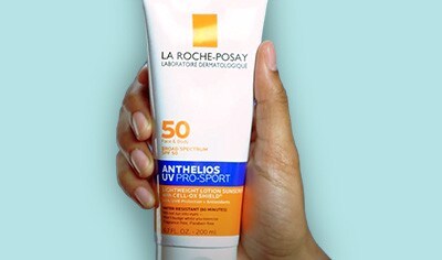 A hand with a medium skin tone holds a white bottle of La Roche-Posay Anthelios UV Pro-Sport Face & Body Sunscreen SPF 50