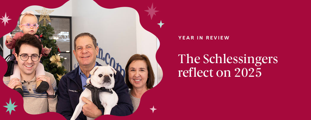 A man in his 30s holds an infant girl on his shoulders while his father and mother smile next to them holding their white pug dog.