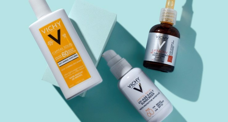 Two bottles of Vichy sunscreen and one bottle of Vichy vitamin C serum on a light blue background.