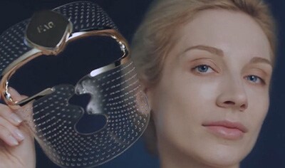 A woman with fair skin and light hair holds the clear and gold FOREO FAQ 202 face mask.