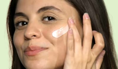 A woman with medium, olive-toned skin and medium brown hair applies Althaea Skin Day Serum to her cheek.