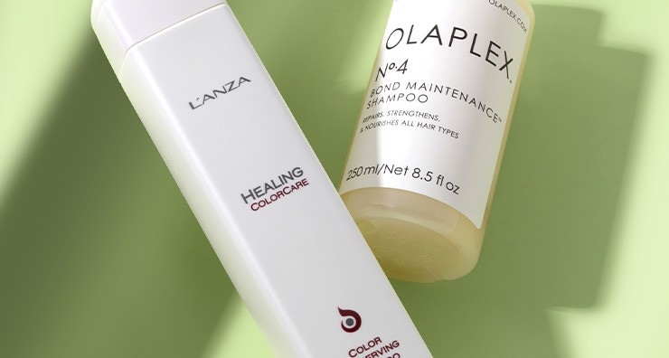 A white L'ANZA shampoo bottle and clear OLAPLEX shampoo bottle with white label pictured on a light green background.