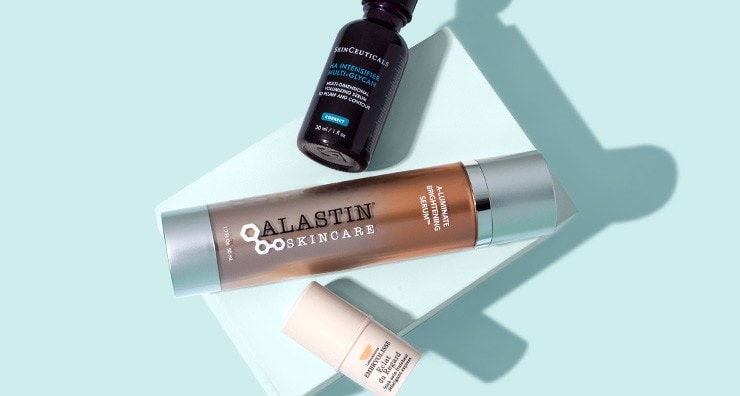 SkinCeuticals HA Intensifier Multi-Glycan Serum, ALASTIN Skincare Brightening Serum and Embryolisse eye treatment on a light blue background.