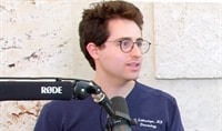 A dermatologist in navy blue scrubs speaking in front of a podcast microphone.