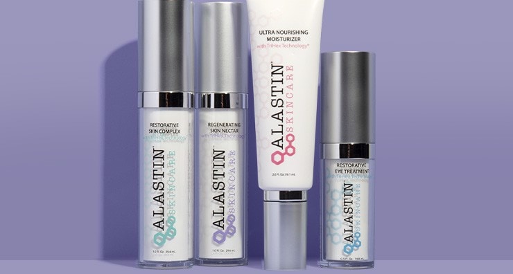 Three clear glass skin care bottles and one tube with silver caps from ALASTIN Skincare on a purple background.