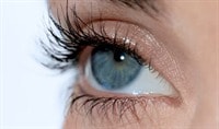 A person with fair skin and blue eyes gazes off into the distance. Their lashes are long, dark and curled.