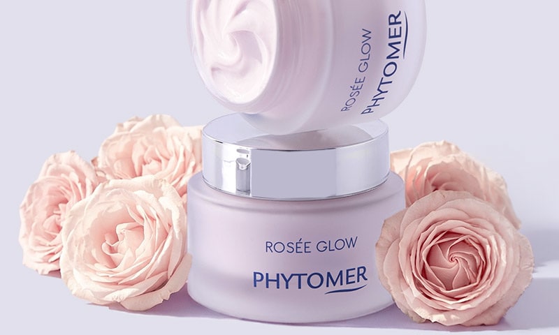 Product pot open to show creamy texture, surrounded by roses