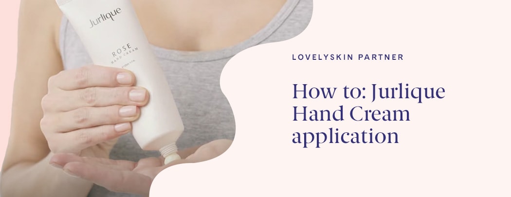 A woman with fair skin, nude colored nails and a grey tank top dispenses Jurlique Rose Hand Cream into her hand.