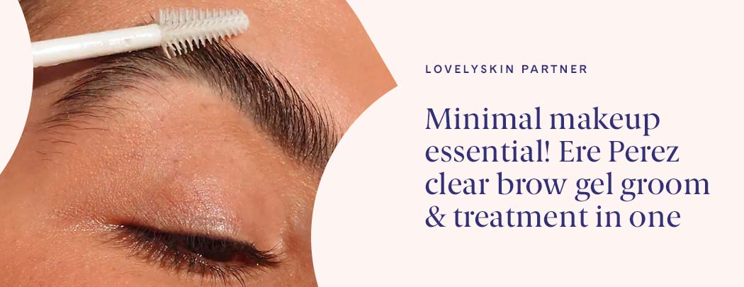 A person with medium, olive-toned skin holds a Ere Perez Aloe Gel Lash & Brow Mascara brush to their eyebrow.