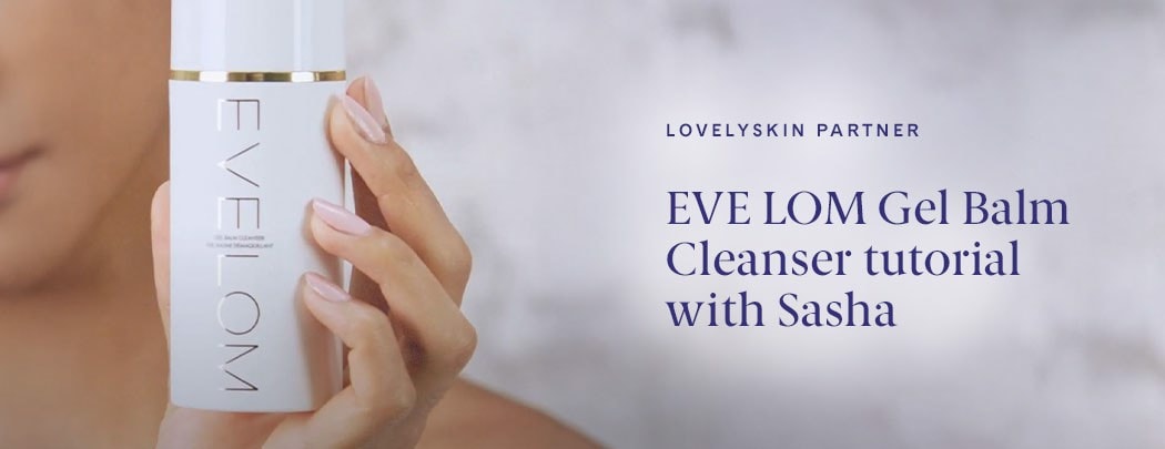 A person with medium skin tone and pink nails holds a white bottle of EVE LOM Gel Balm Cleanser.
