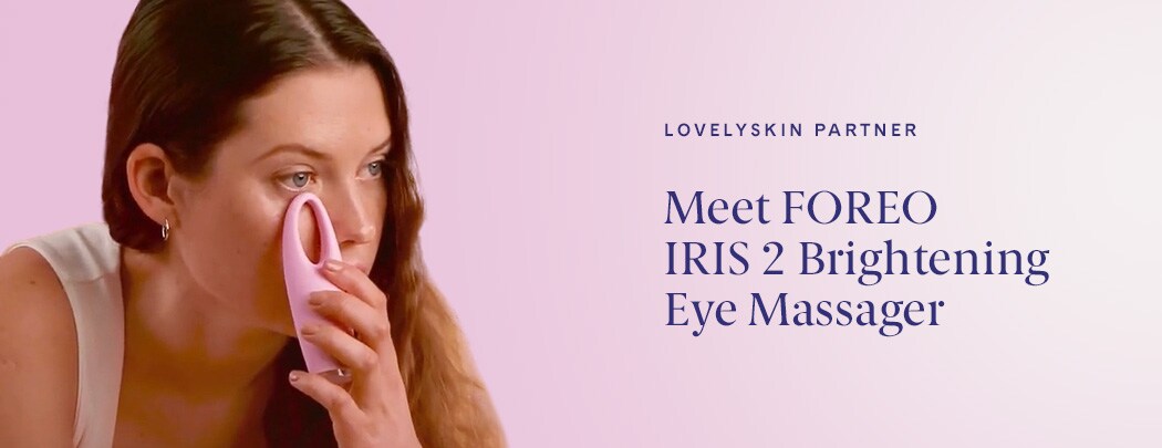 A woman with fair skin and medium brown hair presses the light pink FOREO IRIS 2 device to her eye.