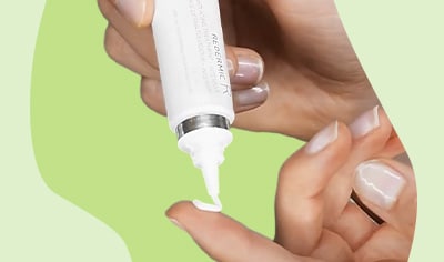 One hand dispensing retinol cream onto an index finger