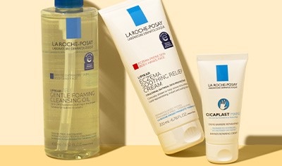 Containers of three La Roche-Posay Lipikar products, including a cleansing oil, moisturizer and hand cream, on an off-white background.