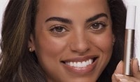 A woman holding a tube of mascara and smiling at the camera.