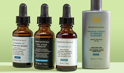 Bottles of SkinCeuticals serums and sunscreen standing up in front of a light green background