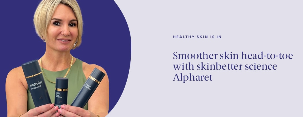 A woman with a light skin tone and a short blonde bob holds three skinbetter science AlphaRet products while smiling.