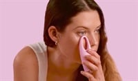 A woman with fair skin and medium brown hair presses the light pink FOREO IRIS 2 device to her eye.