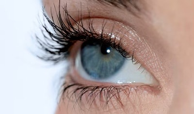 A person with fair skin and blue eyes gazes off into the distance. Their lashes are long, dark and curled.