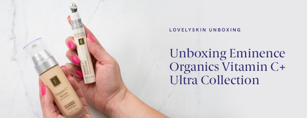 A woman with a light skin tone and pink fingernails holds the Eminence Organics Viamin C+ Serum and Vitamin C+ Eye Cream over a marble background.