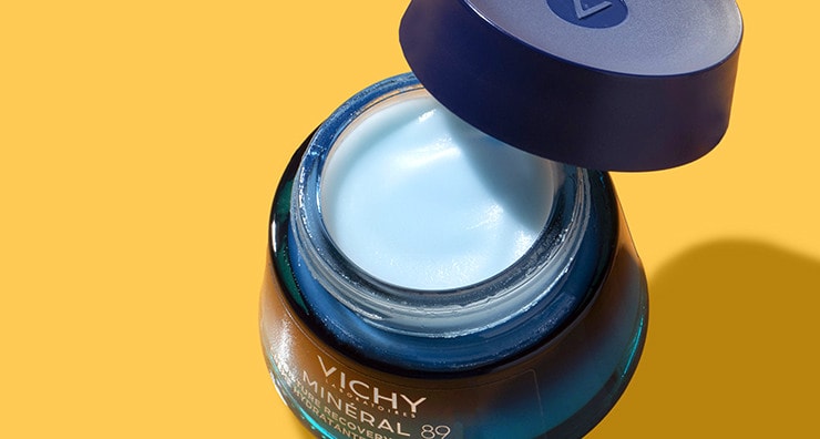 A glass pot of Vichy Mineral 89 Moisture Recovery Night Cream with lid removed and askew pictured on an orange background.
