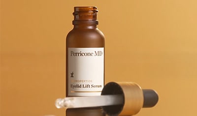 A bottle of Perricone MD Neuropeptide Eyelid Lift Serum sits on a glass top with its dropper is laid next to it. A small amount of product drips out.