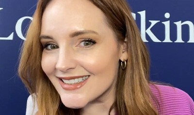 A woman with fair skin and reddish brown hair smiles at the camera wearing a neutral-toned makeup look.