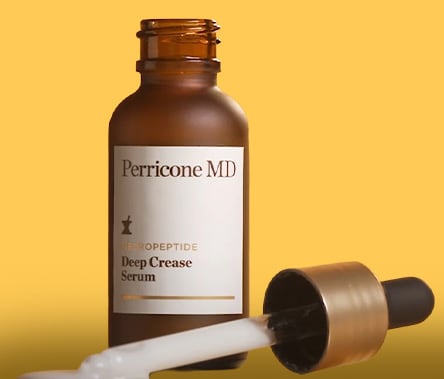 A brown bottle of Perricone MD Neuropeptide Deep Crease Serum sits on clear glass. The dropper is laying next to the bottle with product dispensing.