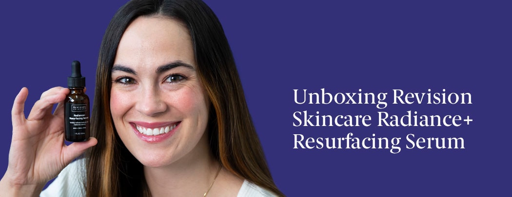 A woman with olive toned skin and dark brown hair smiles while holding a brown serum bottle that has a black label.