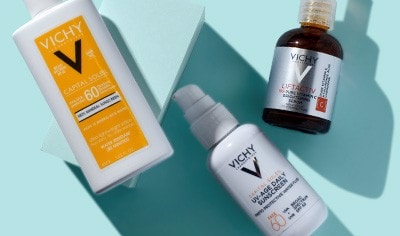 Two bottles of Vichy sunscreen and one bottle of Vichy vitamin C serum on a light blue background.