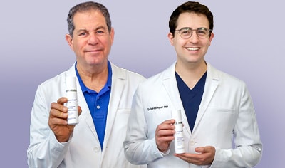 Drs. Joel and Daniel Schlessinger stand next to one another smiling while holding LovelySkin LUXE Firming Peptide Neck Cream.