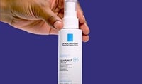 A man's han with a medium-deep skin tone holds a bottle of La Roche-Posay Cicaplast Spray B5 Soothing Repairing Concentrate.
