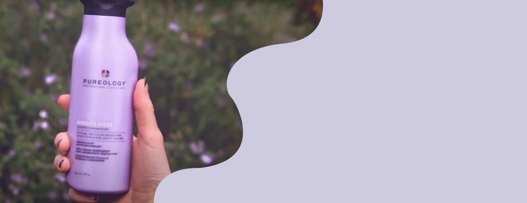 Hand holding a purple bottle of Pureology Hydrate Sheer Shampoo.
