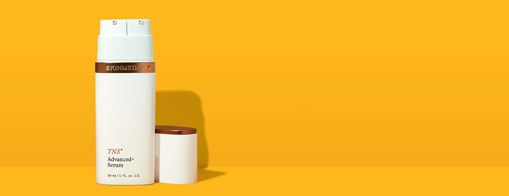 A white bottle with bronze details that reads "TNS Advanced+ Serum" stands on a yellow background.