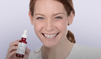 A young woman with fair skin and red hair smiles with a bottle of La Roche-Posay Retinol B3 Serum