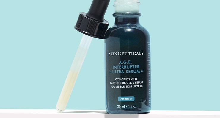 A brown glass bottle of SkinCeuticals A.G.E. Interrupter Ultra Serum with the dropper lid unscrewed and placed next to it on a light blue background.