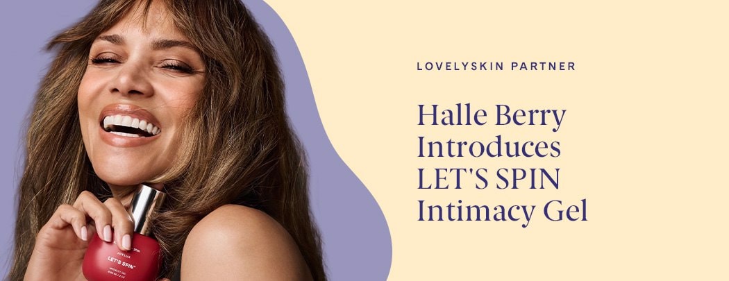 Halle Berry, a woman with medium toned skin and brown hair, smiles while holding a red bottle of Joylux LET'S SPIN Intimacy Gel.