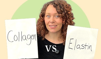 A woman with red curly hair smiles at the camera. She holds a sign in her right hand that says "collagen," and one in her left that says "elastin."